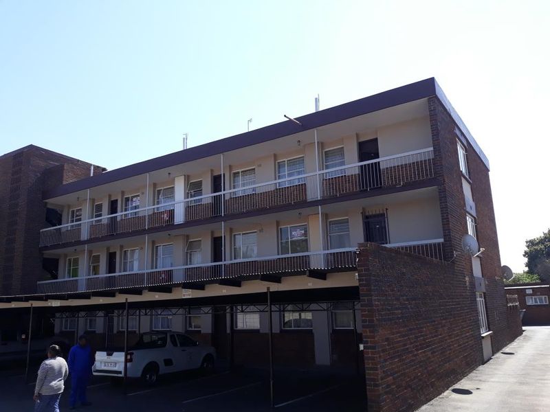 Exterior view of a multi-story apartment building featuring brick facade, private balconies with metal railings, and a covered ground-level carport area.