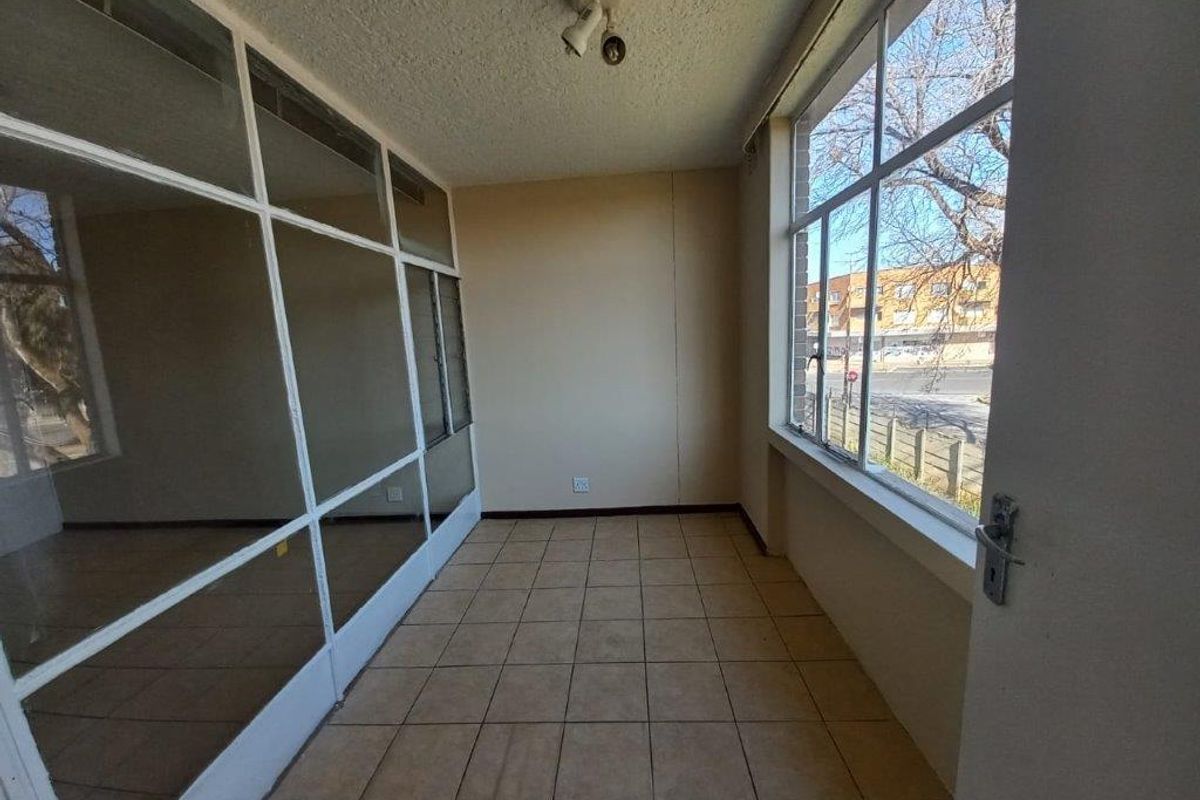 An enclosed balcony or sunroom featuring tiled flooring and large windows, offering a bright, versatile space ready for renovation or staging.