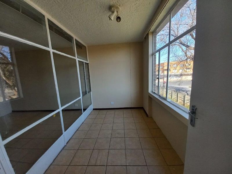 An enclosed balcony or sunroom featuring tiled flooring and large windows, offering a bright, versatile space ready for renovation or staging.