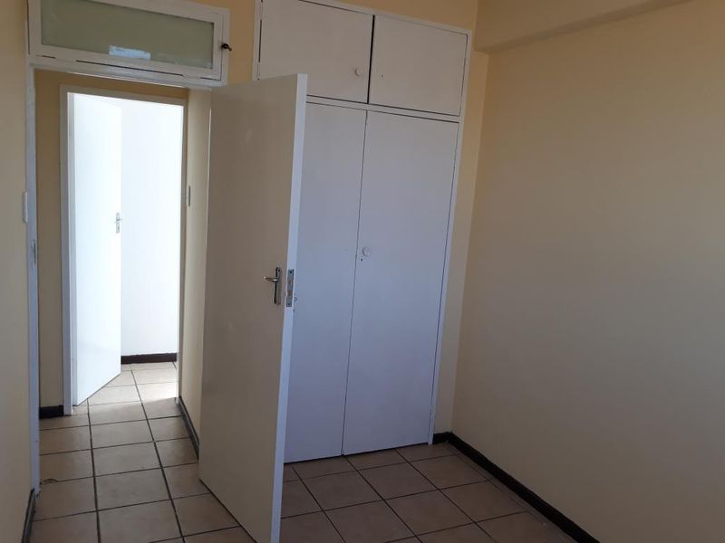 An empty bedroom featuring tiled flooring and built-in cupboards, offering a blank canvas for personalization.