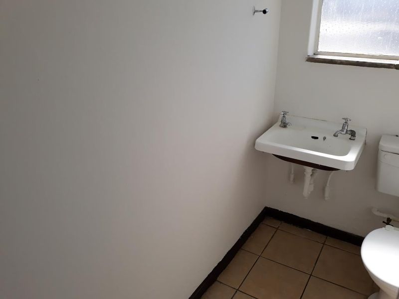 A basic, empty bathroom featuring a wall-mounted basin, toilet, and tiled flooring, requiring cosmetic updates to improve its overall condition.