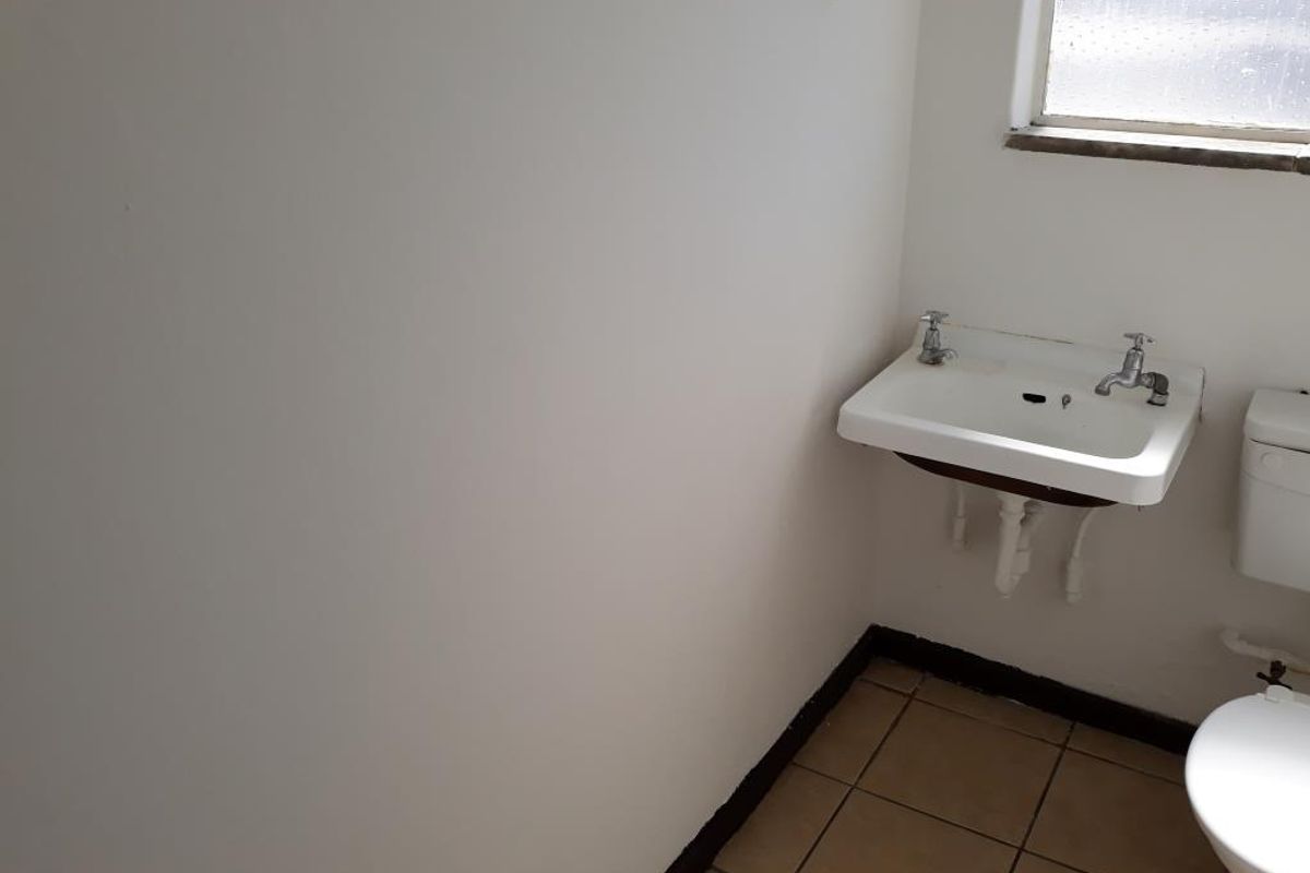 A basic, empty bathroom featuring a wall-mounted basin, toilet, and tiled flooring, requiring cosmetic updates to improve its overall condition.