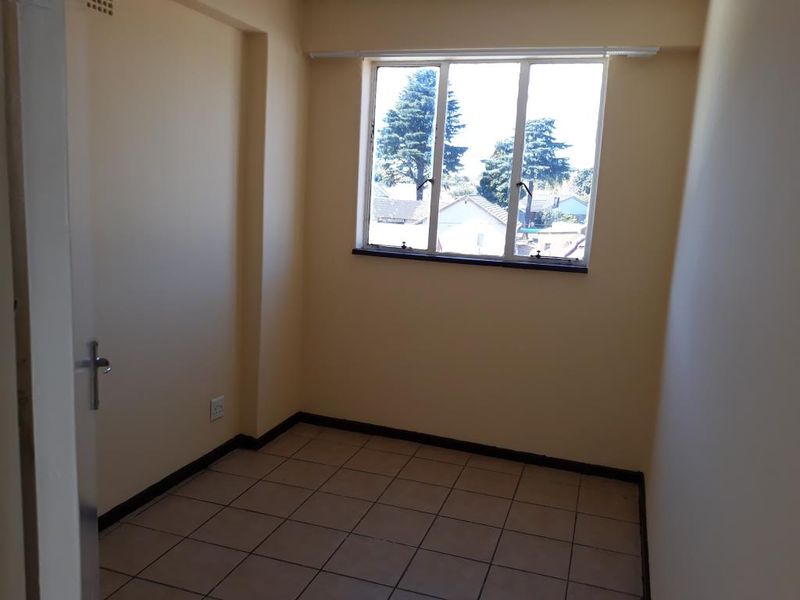An empty bedroom featuring tiled flooring and a window with natural light, providing a blank canvas for personalization.