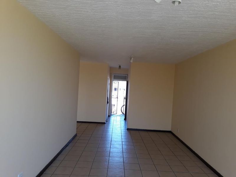 An empty, open-plan living area featuring neutral walls and tiled flooring, leading to an exterior entrance with a security gate.