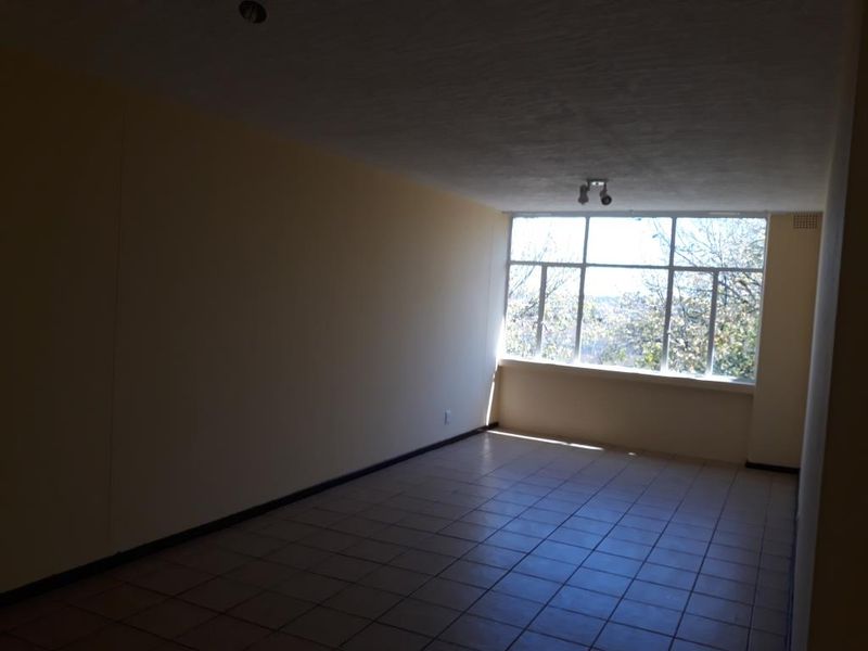 An empty, sunlit living area featuring tiled flooring and a large window with natural views.