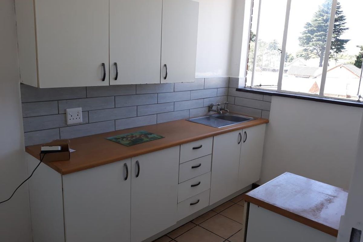 A compact kitchen featuring white cabinetry, a wood-look laminate countertop, stainless steel sink, and modern grey subway tile backsplash with tiled flooring.
