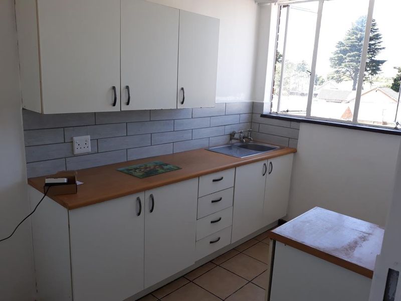 A compact kitchen featuring white cabinetry, a wood-look laminate countertop, stainless steel sink, and modern grey subway tile backsplash with tiled flooring.