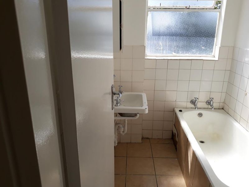 A dated bathroom featuring a standard bathtub, wall-mounted basin, and tiled finishes, requiring cosmetic updates to modernize the space.