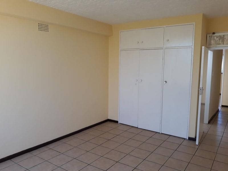 An empty bedroom featuring tiled flooring and built-in cupboards with overhead storage compartments.