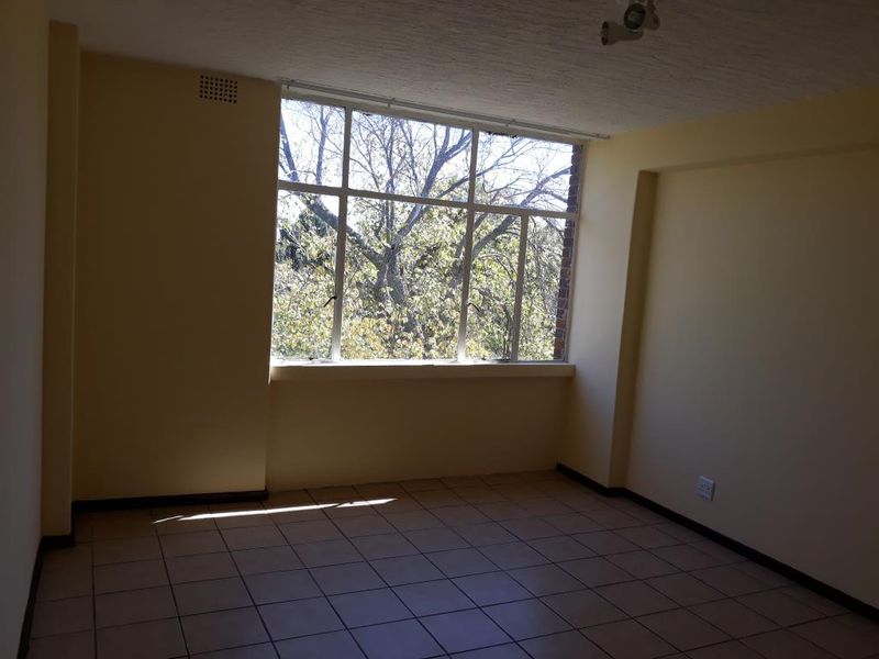 An empty living room featuring large windows that provide natural light, tiled flooring, and a neutral color palette, ready for personalization.