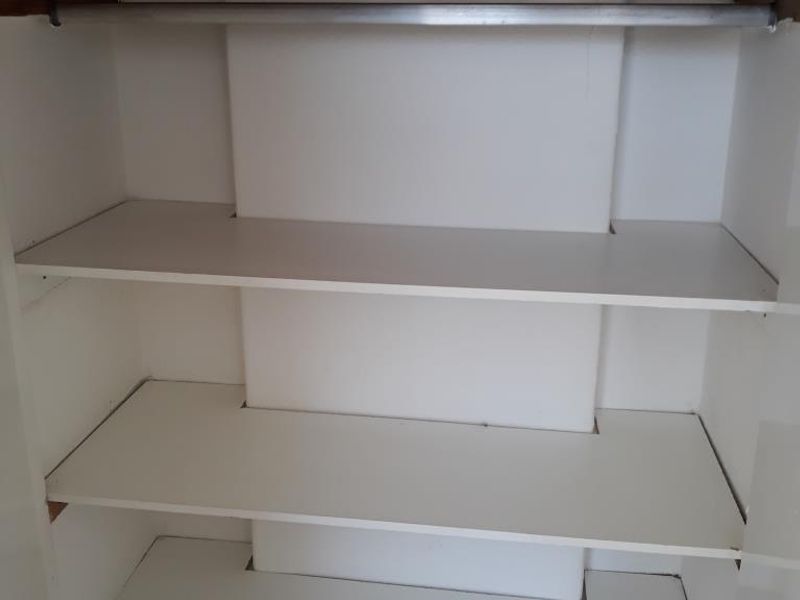 A built-in storage closet featuring multiple shelves and a hanging rail, currently in need of cosmetic finishing and maintenance.