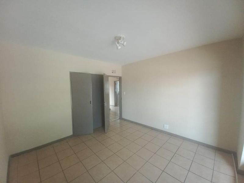 An empty bedroom featuring neutral walls, tiled flooring, and a built-in cupboard, offering a blank canvas for personalization.
