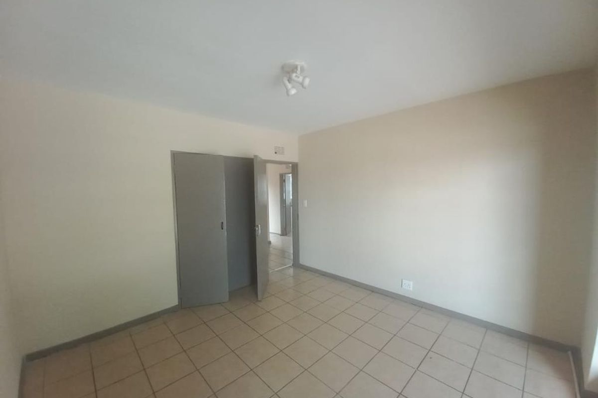 An empty bedroom featuring neutral walls, tiled flooring, and a built-in cupboard, offering a blank canvas for personalization.