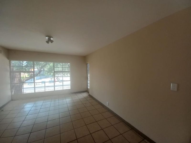 A spacious, empty living area featuring neutral wall tones, tiled flooring, and a large window providing natural light.