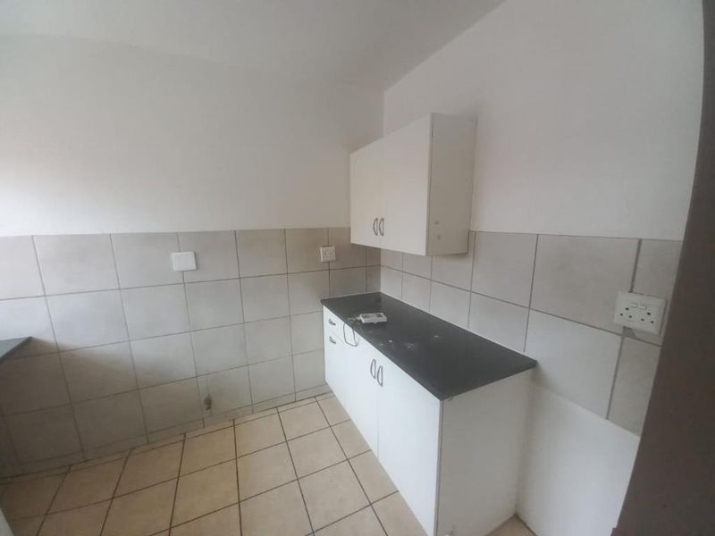 A compact, empty kitchen area featuring tiled splashbacks, laminate countertops, and basic built-in cabinetry, offering a blank canvas for renovation.