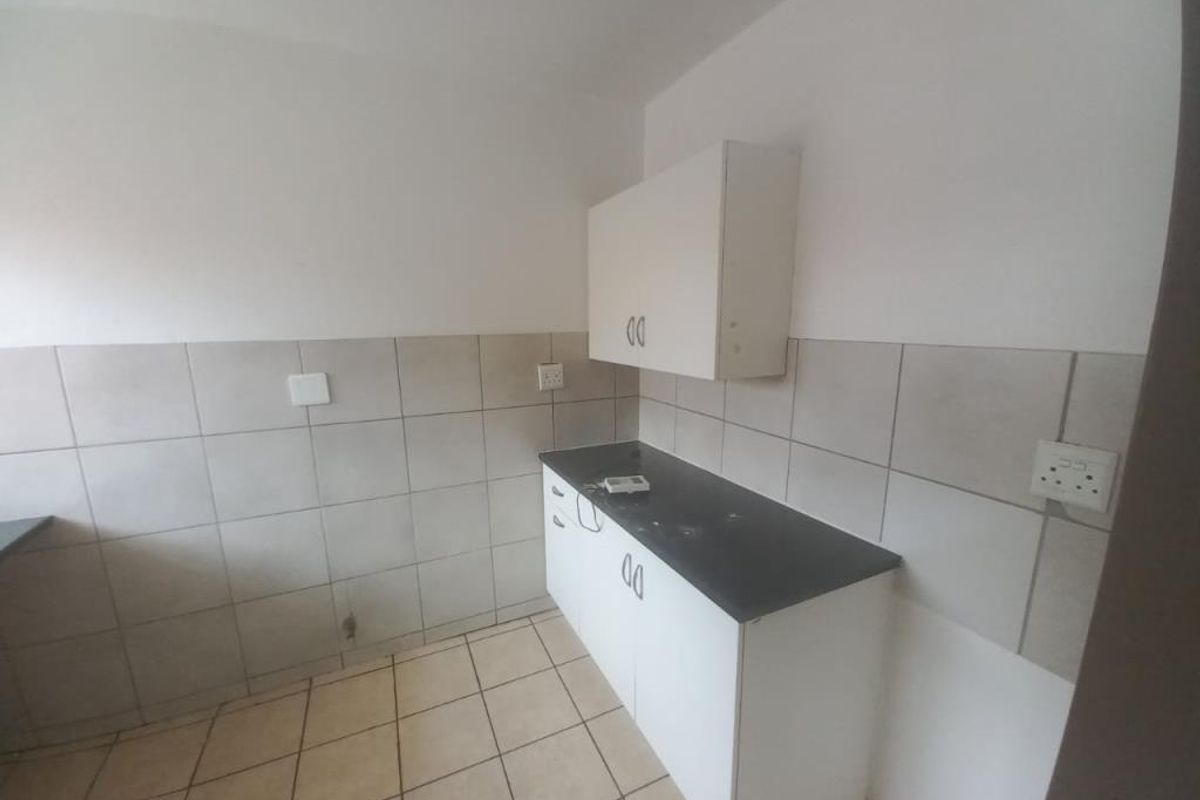 A compact, empty kitchen area featuring tiled splashbacks, laminate countertops, and basic built-in cabinetry, offering a blank canvas for renovation.