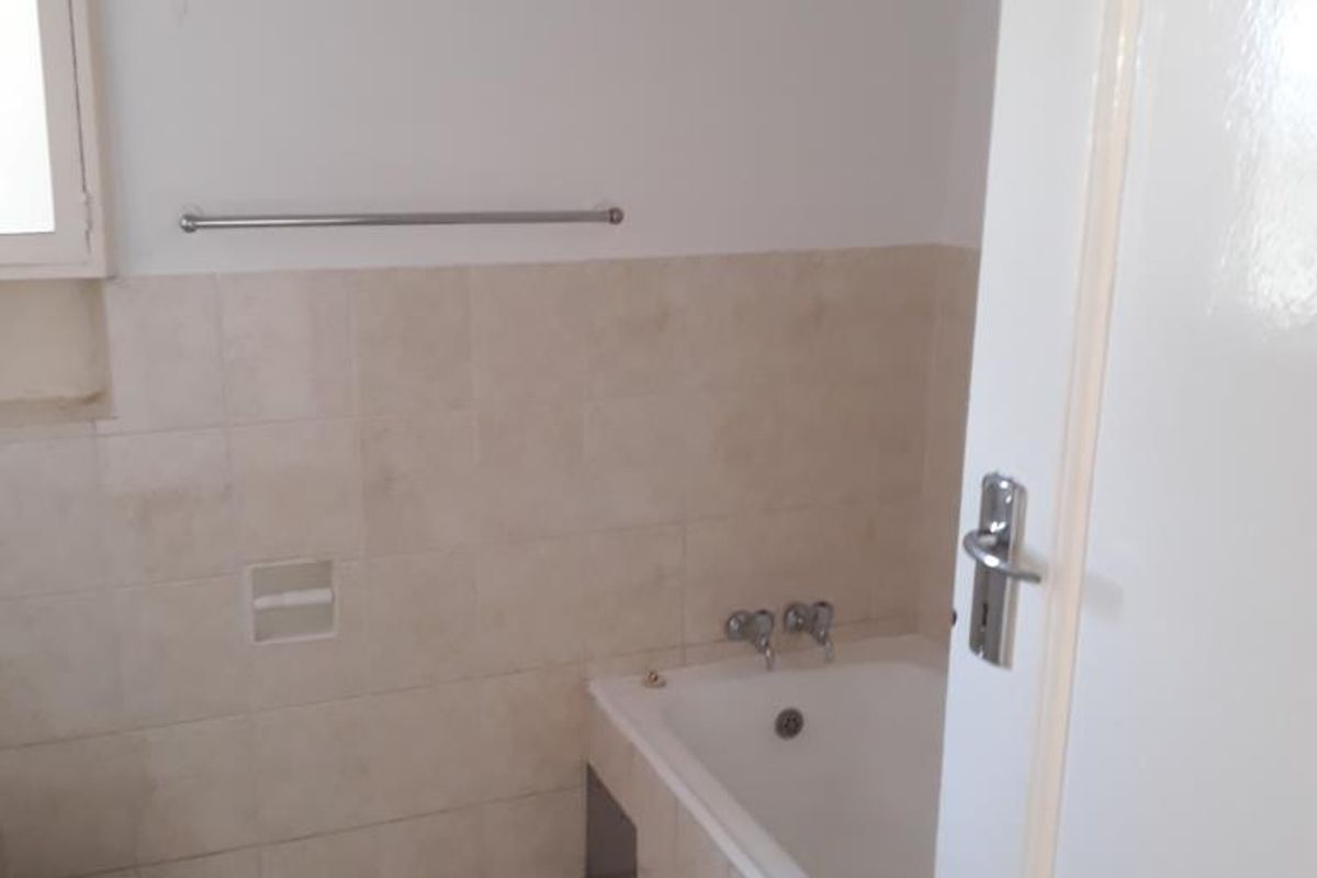 A functional bathroom featuring a built-in bathtub, toilet, and neutral wall and floor tiling.