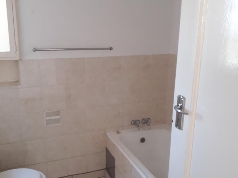 A functional bathroom featuring a built-in bathtub, toilet, and neutral wall and floor tiling.