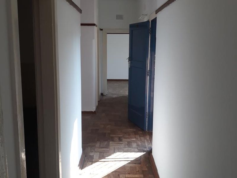 A vacant hallway featuring original parquet flooring and wooden picture rails, connecting multiple rooms within the apartment.