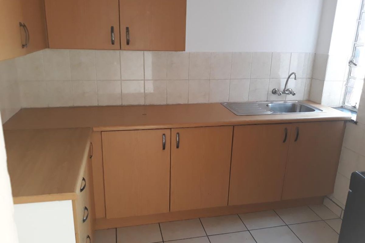 A functional kitchen featuring laminate cabinetry, a stainless steel sink, and tiled surfaces, offering a clean and practical space ready for updates.