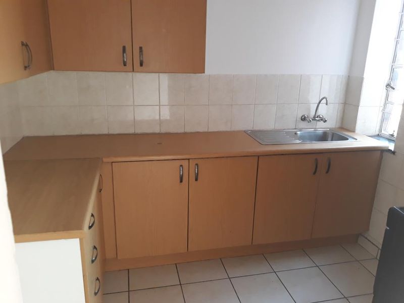 A functional kitchen featuring laminate cabinetry, a stainless steel sink, and tiled surfaces, offering a clean and practical space ready for updates.