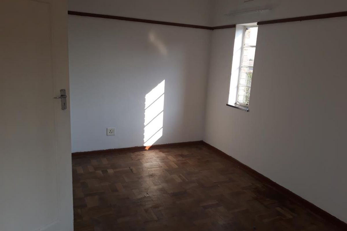 An empty bedroom featuring original parquet flooring, a picture rail, and a steel-framed window, providing a blank canvas for interior design.