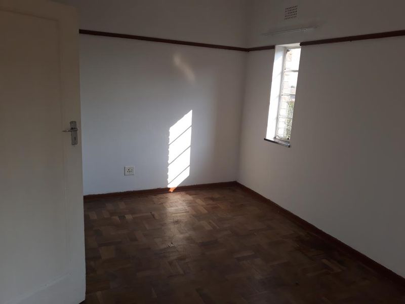 An empty bedroom featuring original parquet flooring, a picture rail, and a steel-framed window, providing a blank canvas for interior design.