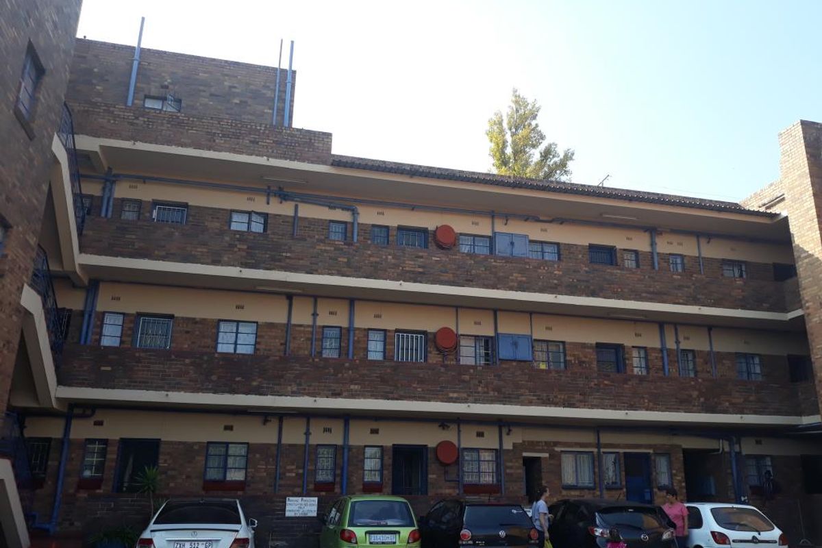 A multi-story apartment building exterior featuring face brick construction, external security bars on windows, and exposed plumbing infrastructure.