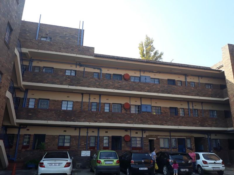 A multi-story apartment building exterior featuring face brick construction, external security bars on windows, and exposed plumbing infrastructure.
