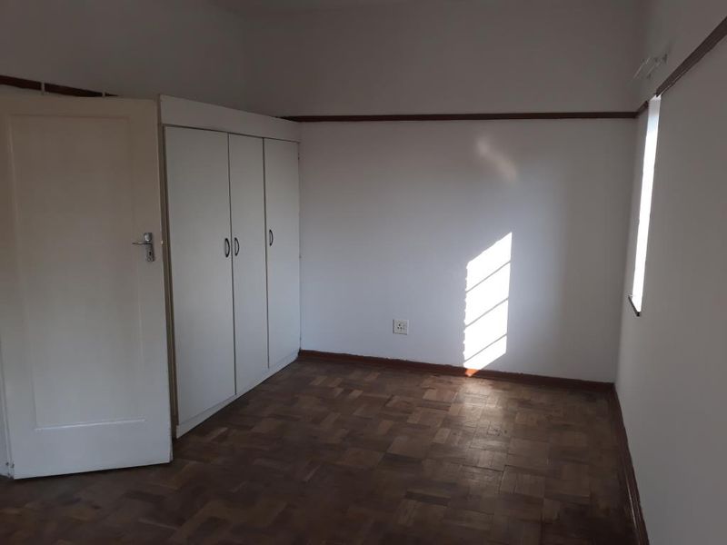 An empty bedroom featuring original parquet flooring, built-in cupboards, and a classic picture rail, offering a blank canvas for renovation.