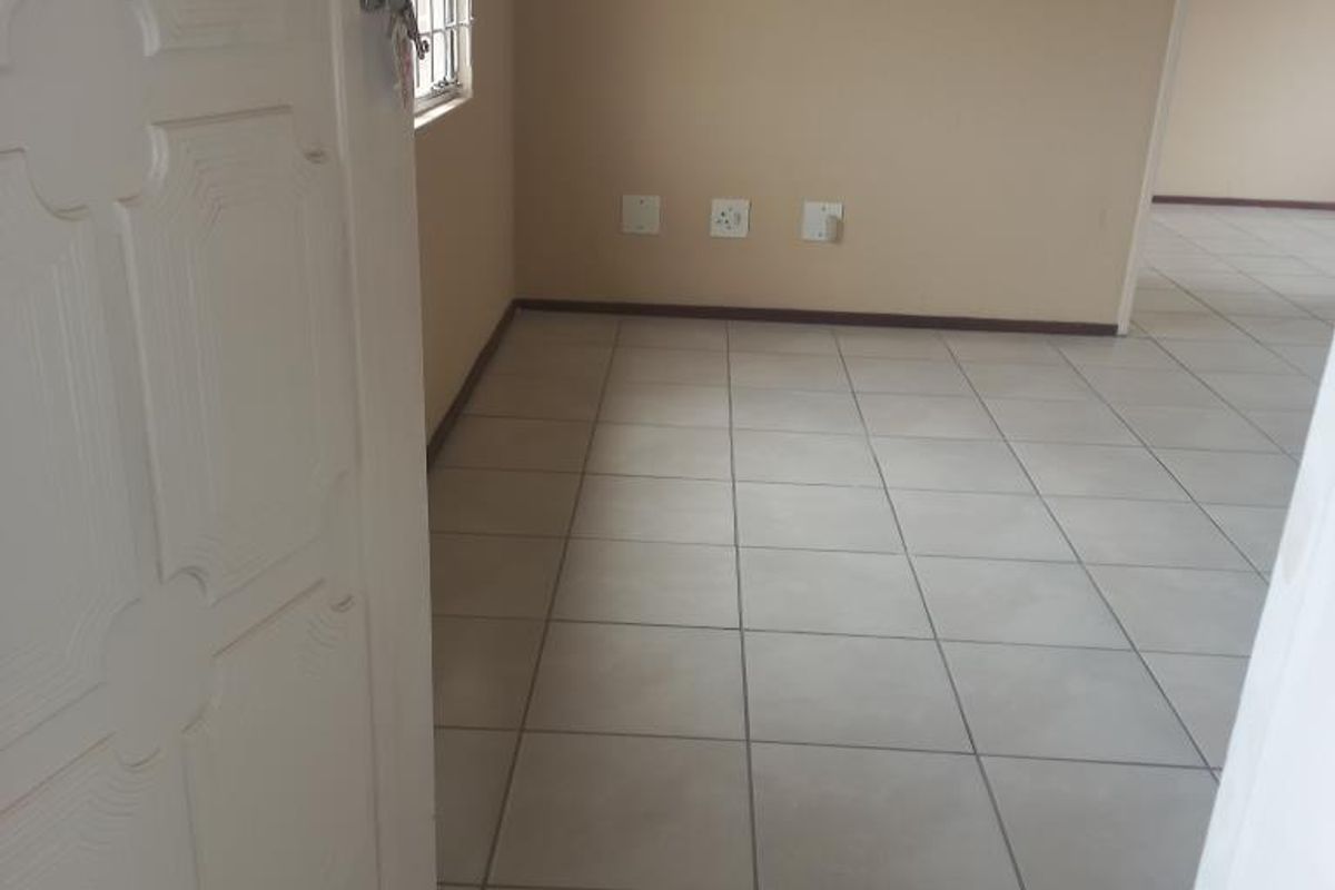 An empty, neutrally painted living area featuring tiled flooring and a security gate at the entrance.