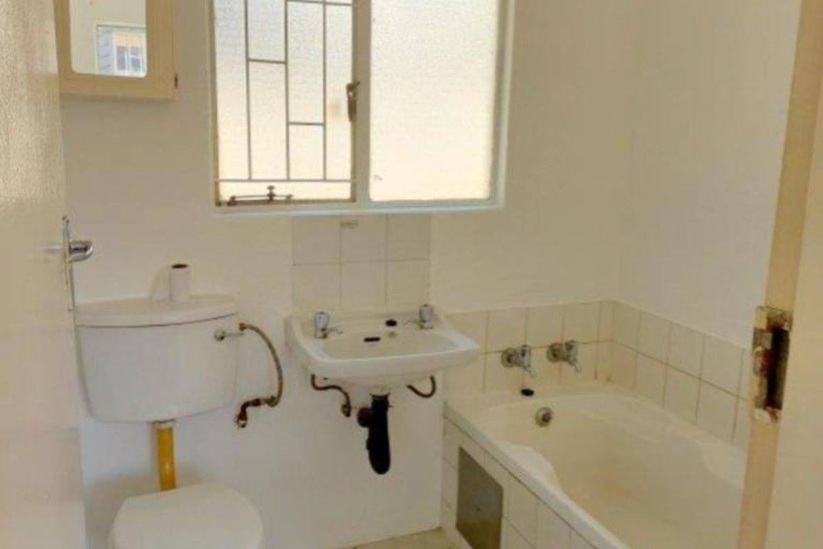 A dated bathroom featuring a standard bathtub, washbasin, and toilet with tiled flooring and splashbacks, requiring cosmetic updates.