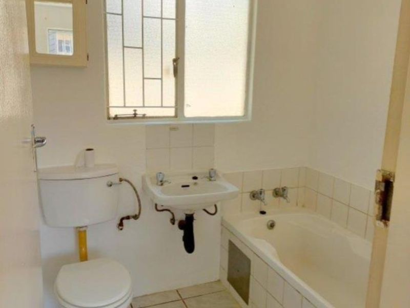 A dated bathroom featuring a standard bathtub, washbasin, and toilet with tiled flooring and splashbacks, requiring cosmetic updates.