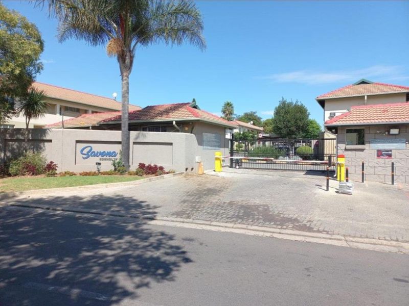 The main entrance to the Savona apartment complex, featuring a secure boom gate, perimeter wall, and paved driveway access.