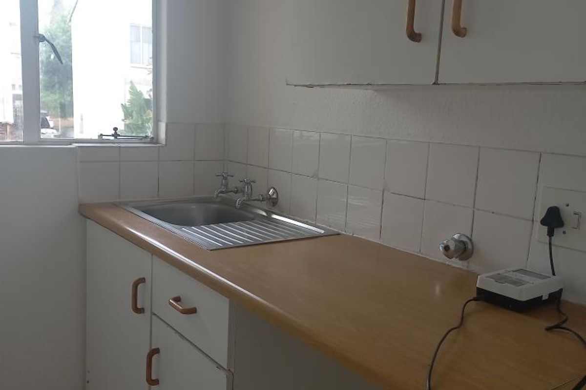 A compact kitchen area featuring laminate countertops, a stainless steel sink, tiled splashback, and built-in cabinetry, offering a functional space ready for modernization.