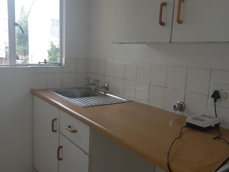 A compact kitchen area featuring laminate countertops, a stainless steel sink, tiled splashback, and built-in cabinetry, offering a functional space ready for modernization.