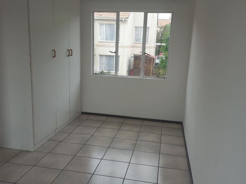 A bright, empty bedroom featuring neutral tiled flooring and built-in cupboards, offering a clean canvas for personalization.