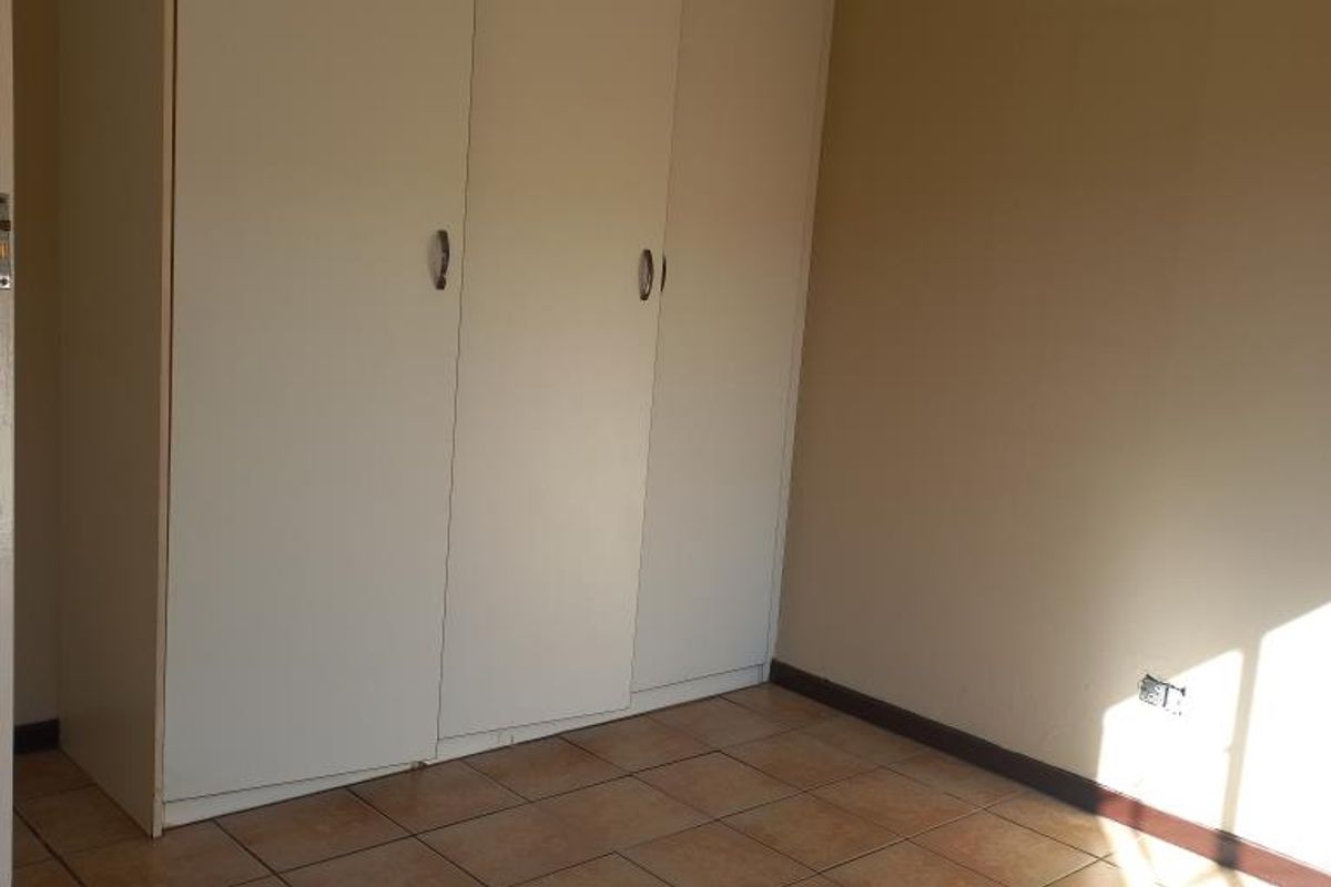 A clean, empty bedroom featuring neutral walls, tiled flooring, and built-in cupboards, offering a blank canvas for personalization.