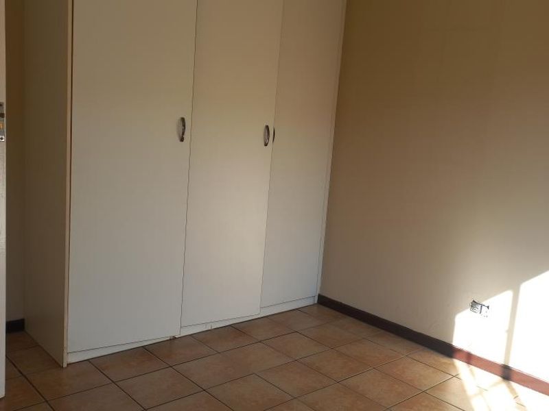 A clean, empty bedroom featuring neutral walls, tiled flooring, and built-in cupboards, offering a blank canvas for personalization.