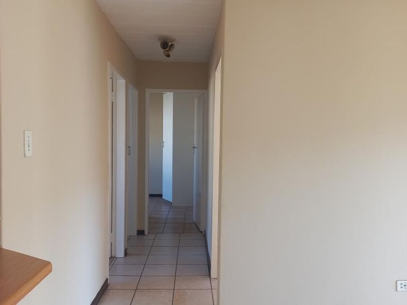 A vacant hallway featuring ceramic floor tiles, neutral wall paint, and multiple internal door access points.