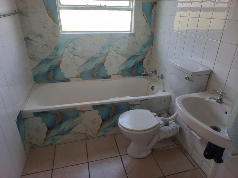 A dated bathroom featuring a bathtub, pedestal basin, and toilet with exposed plumbing and decorative wall tiling.