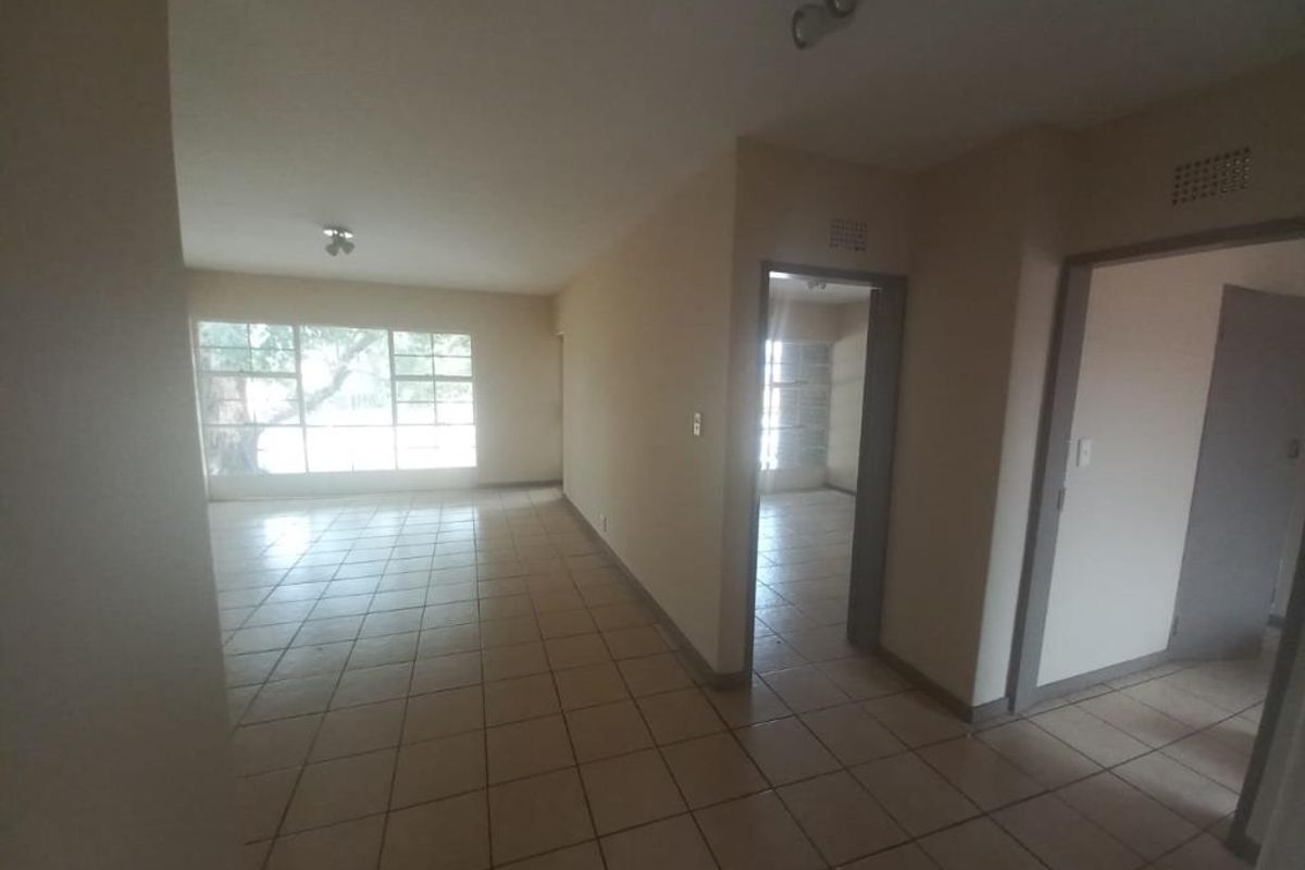 An empty, open-plan living area featuring neutral tiled flooring and large windows, providing a blank canvas for potential interior design and renovation.