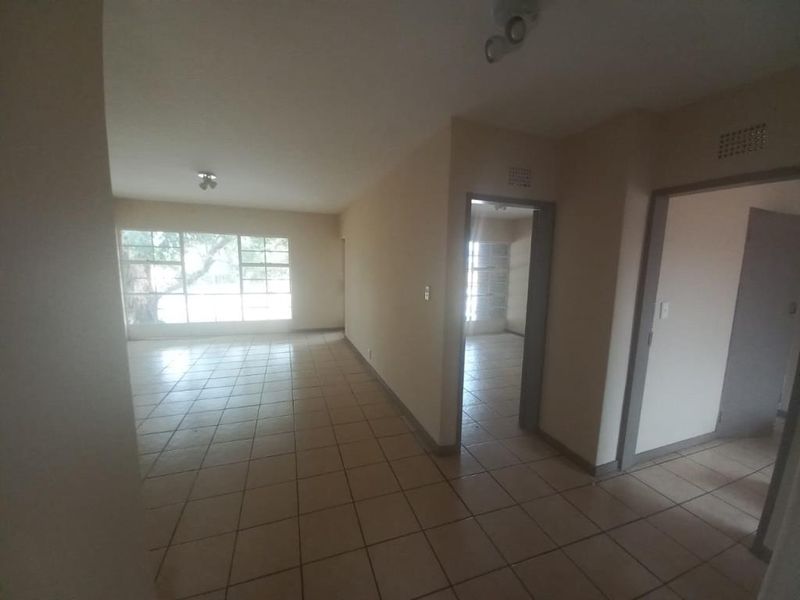 An empty, open-plan living area featuring neutral tiled flooring and large windows, providing a blank canvas for potential interior design and renovation.