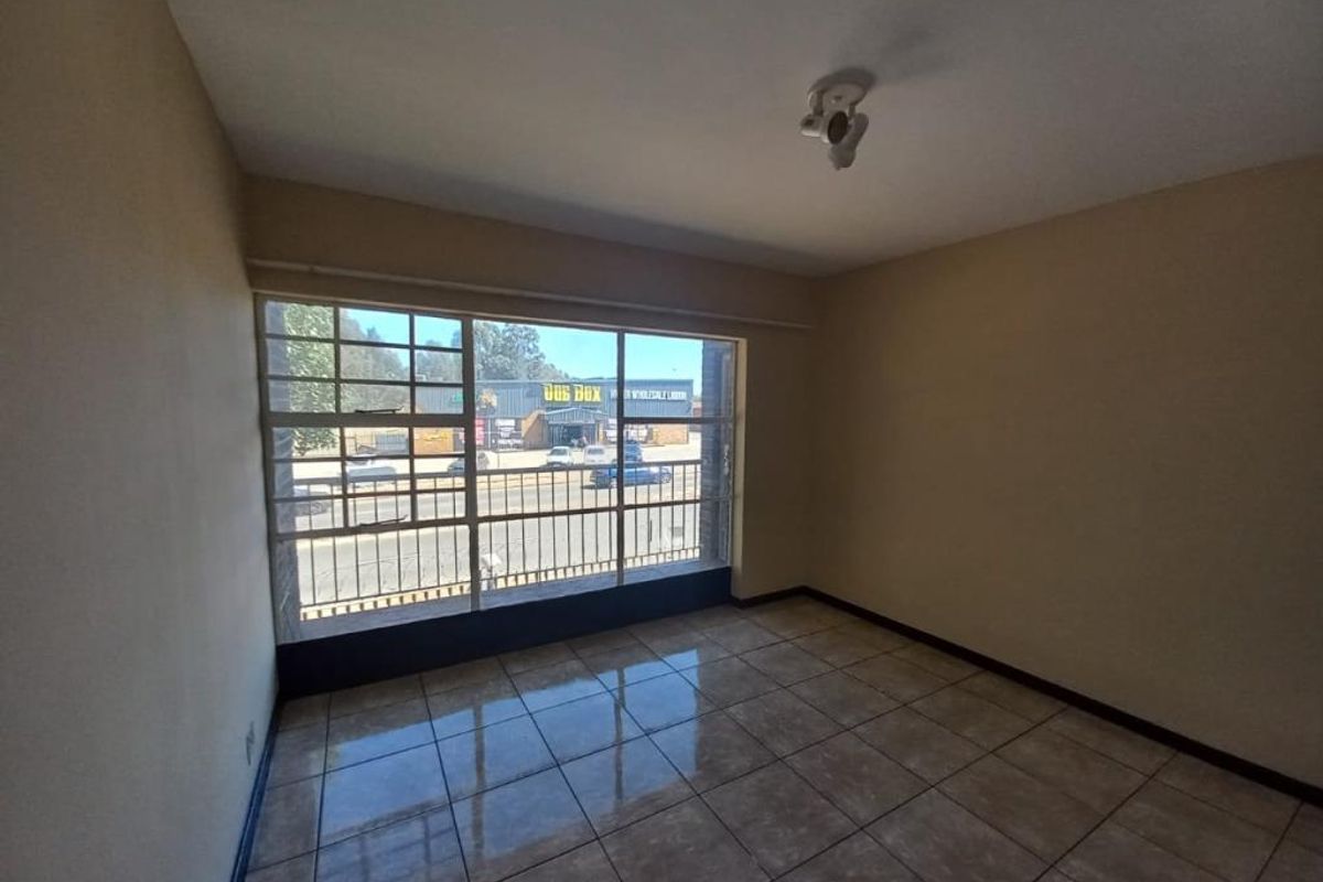 An empty living room featuring large metal-framed windows, ceramic tiled flooring, and neutral wall finishes, offering a blank canvas for interior design.