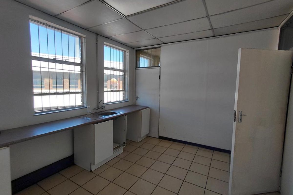 A functional commercial kitchenette featuring a stainless steel sink, laminate countertop, tiled flooring, and security bars on the windows.