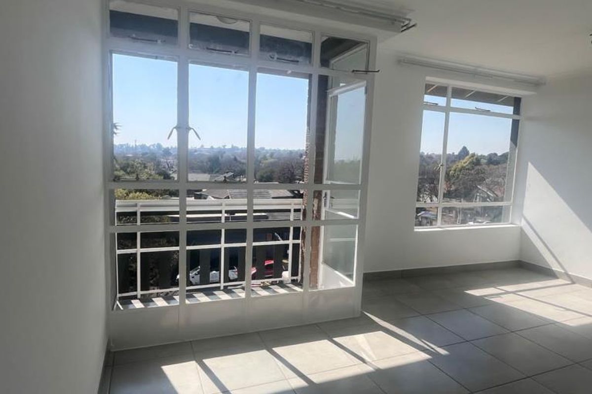 A bright, empty living area featuring large windows, tiled flooring, and direct access to a balcony with neighborhood views.