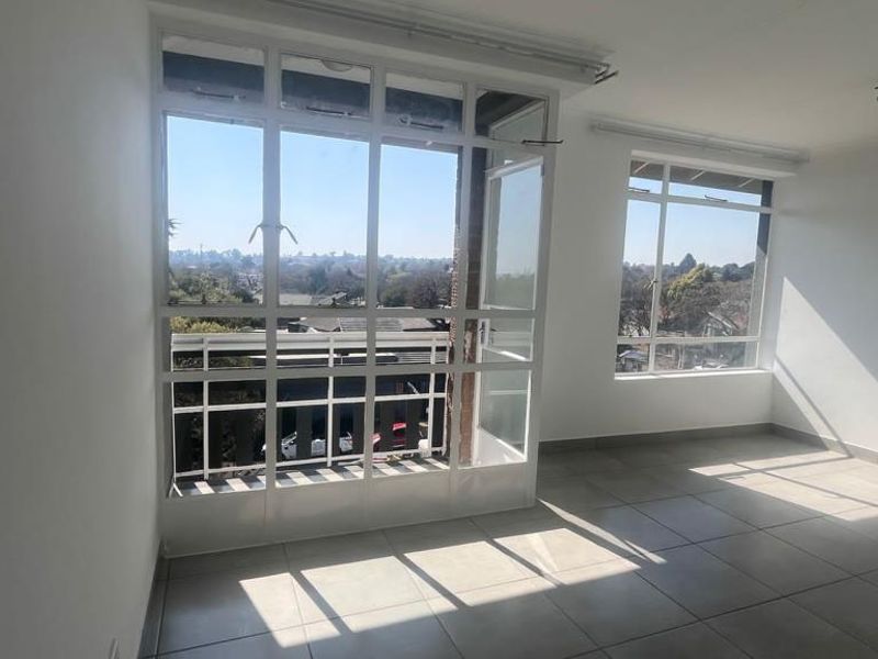 A bright, empty living area featuring large windows, tiled flooring, and direct access to a balcony with neighborhood views.
