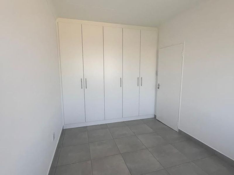 A clean, empty bedroom featuring neutral tiled flooring and ample built-in cupboard storage space.