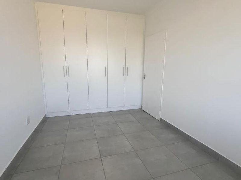 A clean, empty bedroom featuring neutral grey floor tiles and ample built-in cupboard storage space.