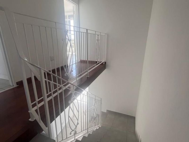 A bright, modern staircase featuring a white metal balustrade, wooden landing flooring, and neutral tiled steps leading to an upper level.